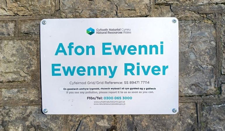 A sign on a wall next to a river with information on how to report suspected river pollution